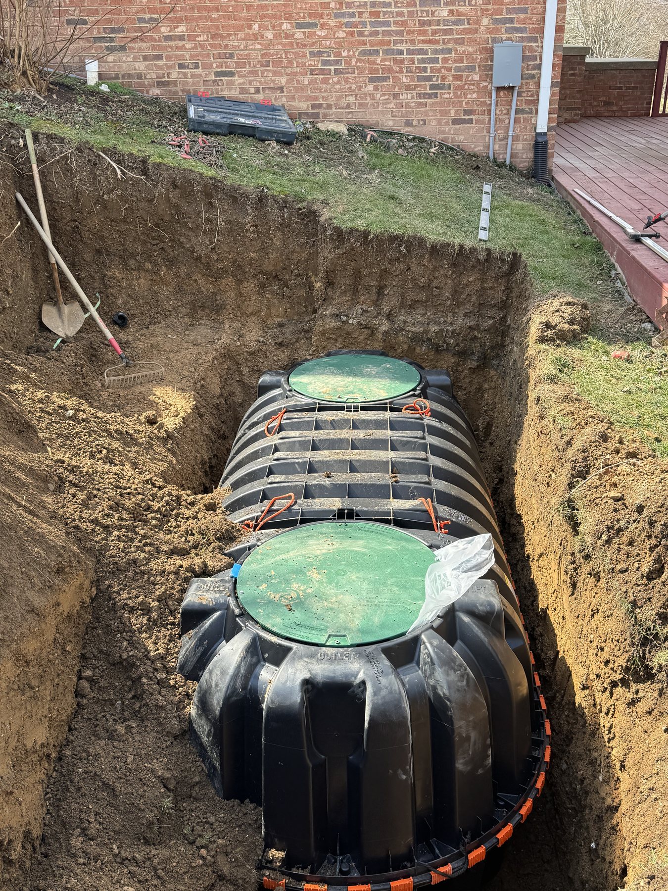 Septic tank and green access risers being installed in an excavated trench.